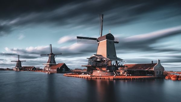 A group of cyclists traveling through a scenic route along beautiful windmills and canals in Netherlands A group of cyclists traveling through a scenic route along beautiful windmills and canals in Netherlands